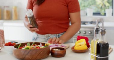 Asyalı kadın biber öğütücüsüne uzanıyor. Beyaz mutfakta biberli ve zeytinyağlı baharat salatası. Sağlıklı beslenme, aşçılık, taze malzemeler, mutfak gereçleri, doğal ışıklandırma, yaşam tarzı, ev yemeği.