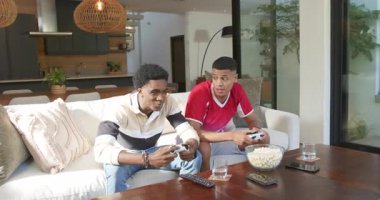 İki yetişkin erkek arkadaş kanepede maç başlıyor, kutluyor, patlamış mısır yakalıyorlar. Gündelik, boş, eğlence, arkadaşlık, şakacı, modern, rahat