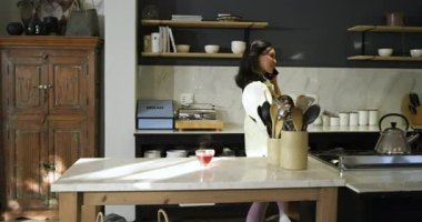 Bebek taşıyan orta yaşlı bir kadın mutfakta akıllı telefonlara cevap verirken, fotokopi odasında. Annelik, çoklu görev, yerli, çağdaş, yaşam tarzı, bakım, konfor