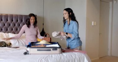 Renkli giysiler tutan bir kadın otel odasındaki açık bavullarda eşyaları ayırıyor, fotokopi çekiyor. Seyahat, eşya, gardırop, yaşam tarzı, organizasyon, iç mekan, günlük