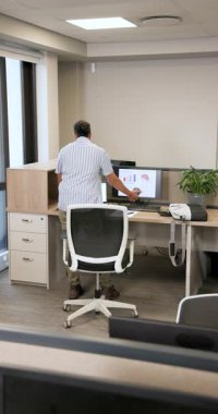 Ofis çalışanı çalışma kabinine girdi. Dosyaları gözden geçiriyor. Dizüstü bilgisayarlarını topluyor ve iş arkadaşlarını teslim etmek için bitki ekiyor. Profesyonel, işbirlikçi, ergonomik, dijital, çalışma alanı, organizasyonel, dikey video