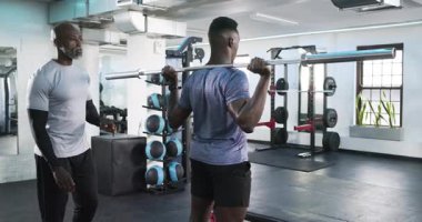 Alıştırma tesisinde halterle çömelmiş halterlere rehberlik eden bir antrenör. Spor, güç, antrenörlük, spor, atletizm, egzersiz, kararlılık