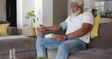 Kanepeye yerleşmek, Afrika kökenli Amerikalı kıdemli bir adamın kelepçeleri takması, kontrol için dijital monitöre başlaması. Sağlık, sağlık, rahatlama, ev bakımı, tıbbi, dijital, konfor