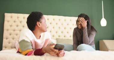 Hintli ve Afrikalı Amerikalı arkadaşlar hayal kırıklıklarını işaret ediyorlar, yataktaki akıllı telefonu görmezden geliyorlar. Arkadaşlık, iletişim, duygular, gündelik, çeşitlilik, ifade, rahatlama