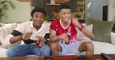 Çeşitli erkek arkadaşlar oturma odasında spor maçına tepki verirken gazoz içip pizza yiyorlar. Sıradan, yoldaşlık, rahatlama, kutlama, eğlence, çağdaş, canlı