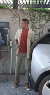 Garaj altında EV vagonuna doğru yürüyen bir çift, kablo yerleştiriyorlar, telefonları dinliyorlar ve selfie çekiyorlar. Çağdaş, yaşam tarzı, modern, çevre dostu, kentsel, neşeli, dikey video