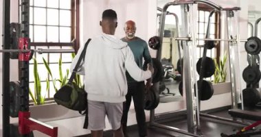 Spor çantasıyla spor salonuna girmek, siyah erkek müşteri antrenörüne sarılmak, çömelme yerinde ısınmak. Fitness, strength, training, motivasyon, wellness, Health, Gym