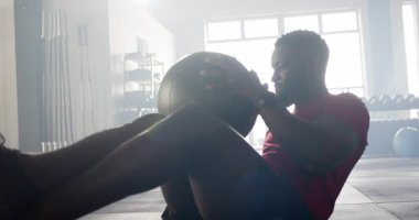 Göğsünde siyah tıp topu tutan Afro-Amerikan bir adam, gövdesini güçlendirmek için spor salonunda kıvrılıyor. Zindelik, güç, egzersiz, direnç, eğitim, sağlık, aktif