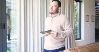 Olgun Asyalı adam okumak için oturma odasına giriyor, kanepeye bardakları yerleştiriyor ve kitap sayfalarını çeviriyor. Rahat, rahat, modern, sofistike, rahatlama, yaşam tarzı, huzur