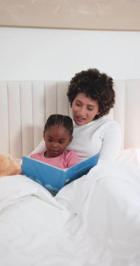 Çeşitli anne ve kızlar oyuncak ayının yanında masal kitabı açıp yatakta masal okuyorlar. Aile, yetiştirme, hayal gücü, rahatlık, bağlanma, hikaye anlatma, dikey video