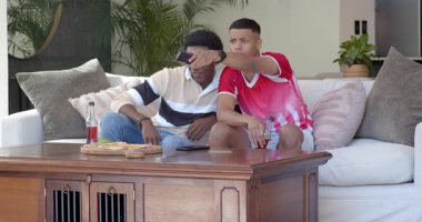 İki erkek arkadaş futbol maçı izleyip uzaktan kumanda alıyor, gazoz yudumluyor, tezahürat yapıyor, top atıyor. Sıradan, yoldaşlık, eğlence, canlı, boş, sosyal, yaşam tarzı.