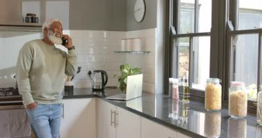 Kıdemli Afrikalı Amerikalı telefon görüşmelerine cevap veriyor mutfak tezgahındaki bilgisayardan, kopyalama alanından. Profesyonel, teknoloji, ev, yaşam tarzı, modern, iletişim, konfor