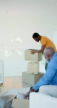 Dikey video: Oturma odasında kutu taşıma oğlu yastıkları açıyor ve baba kanepeyi düzenliyor. Aile, yenileme, iç dekorasyon, ev dekorasyonu, yapıştırma, modern, dikey video
