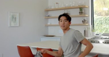 Asyalı bir adam mutfak tezgahında kamuflaj ceketi taşıyor, teftiş için oturuyor ve ceketini örtüyor. Gündelik, modern, yaşam tarzı, iç mekan, çağdaş, moda, rahatlama