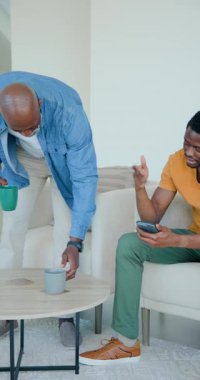 Dikey video: Yaşlı baba eve giriyor telefonda üzgün oğlu fark ediyor rahatlamak için kupa teklif ediyor. Aile, akıl hocalığı, iletişim, sıcaklık, rahatlama, ev içi, dikey video