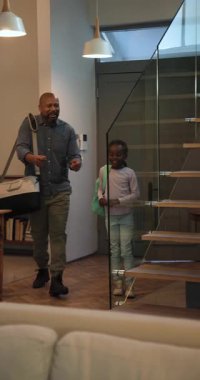 Dikey video: Afrikalı Amerikalı baba ve kız içeri giriyor, televizyon izlemek için kumandaya basıyor. Aile, ev, oturma odası, tahviller, konfor, yaşam tarzı, dikey video