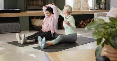 Kıdemli eğitmen, oturma odasındaki paspasların üzerinde durabilmek için katılımcıya yol gösteriyor. Sağlık, esneme, yoga, rahatlama, kıdemli fitness, uyum, farkındalık.