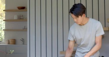 Ekran dışından gelen sinyalleri duyan Asyalı bir adam veranda tezgahına yaslanıyor, gülümsüyor ve gülüyor. Rahat, rahat, yaşam tarzı, minimalizm, ev, iç, sıcaklık