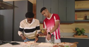 Marble Island 'da akıllı telefon tarifini takip eden ve pizza için hamur üzerinde kaşık peynir yiyen erkek arkadaşlar. Aşçılık, aşçılık, işbirliği, modern, gurme, ev, takım çalışması