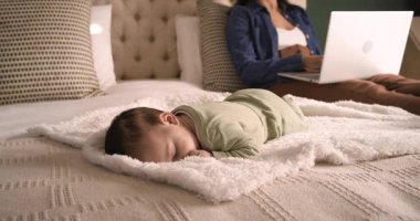 Bebek yatakta kestirirken Asyalı anne dizüstü bilgisayarda yazı yazıyor, kamera yatak başlığına geri çekiliyor. Annelik, çoklu görev, rahatlama, konforlu, evcil, iş hayatı dengesi, yetiştirme