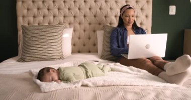 Dizüstü bilgisayarı kucağına koyduktan sonra Afrikalı Amerikalı anne bebeği izlerken yatakta yazı yazıyor. Annelik, çoklu görev, ev idaresi, yetiştirme, rahatlık, aile içi, gündelik