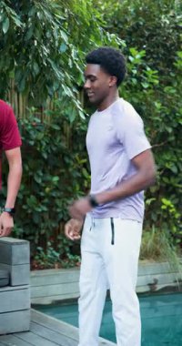 Erkek arkadaşlar saat takıyor güvertede sırt çantasının yanında el çırpıyorlar ve şınav çekiyorlar. Fitness, yoldaşlık, açık hava, aktivite, sağlık, boş zaman, dikey video