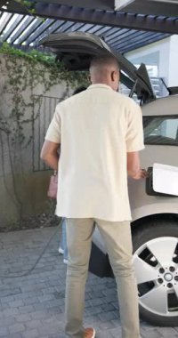 Afro-Amerikalı çift, garajın altına SUV park ediyor, bakkaldan alışveriş yapıyor ve EV 'yi şarj ediyor, kopyalama alanı. Modern, yaşam tarzı, ulaşım, çevre, teknoloji, gündelik, dikey video