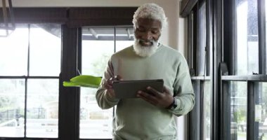 Ofise girerken, kıdemli Afrikalı Amerikalı adam güncellemeleri okumak için tableti tıklatıyor, dışarı bakıyor, gülümsüyor. Teknoloji, profesyonel, modern, iş, gevşeme, çağdaş, çalışma