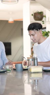 Çeşitli erkek arkadaşlar yemek çubukları kullanıyor, Fransız kahvesi dolduruyor, yumurtaları baharatlı hale getiriyor, barda gülüyorlar. Kahvaltı, yoldaşlık, modern mutfak, gündelik, boş zaman, keyiflilik, dikey video