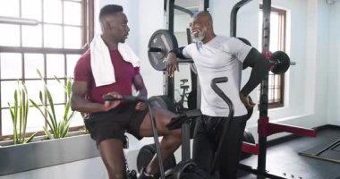 Spor salonundaki aradan sonra Afrikalı Amerikalı müşteri hava bisikletini durdurup antrenör tavsiyesi almak için su alıyor. Eğitim, fitness, koçluk, motivasyon, sağlık, egzersiz, güç