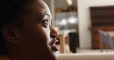 Afro-Amerikalı kadın süprizi gülümsemeye çeviriyor, evdeki büfenin yanında otururken, boşluğu kopyalıyor. Portre, mutluluk, memnuniyet, rahatlama, iç mekan, sıcak aydınlatma, pozitif ruh hali