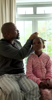 Dikey video: Saç için tarak kullanmak, Afrikalı Amerikalı bir babanın yatakta kızını kucaklaması ve gıdıklaması. Aile, yetiştirme, bağlanma, yakınlık, sevgi, ebeveynlik, dikey video