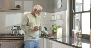 Laptop ekranına baktıktan sonra olgun bir Afro-Amerikan erkeği mutfakta kahve yazıp yudumluyor. Paslanmaz çelik, sade, rahat, odaklanma, verimlilik, rahatlama, sabah