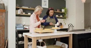 Çeşitli bayan arkadaşlar tezgaha pasta koyar, mutfak adasında beyaz kremayla pasta süslerler. Pişirme, işbirliği, işçilik, kırsal, ev yapımı, aşçılık, arkadaşlık