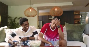 Kanepedeki komik oyun kusuruna tepki verirken çeşitli erkek arkadaşlar patlamış mısır alıyor. Gündelik oyun, arkadaşlık, eğlence, yaşam tarzı, modern mobilya, canlı, dinamik