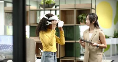 Tablete yanıt veren çeşitli kadın iş arkadaşları ofiste kulaklık kullanarak sanal gerçeklik dünyasını keşfediyorlar. İşbirliği, yenilik, teknoloji, sanal gerçeklik, yenilenebilir enerji, takım çalışması, modernizasyon