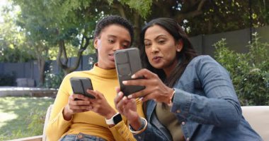 Çeşitli bayan arkadaşlar akıllı telefonları kahkahalarla paylaşan arkadaşlarını arka arkaya verandada otururken görüyorlar. Gündelik, dostluk, açık hava, rahat, enerjik, iletişim, bağ.