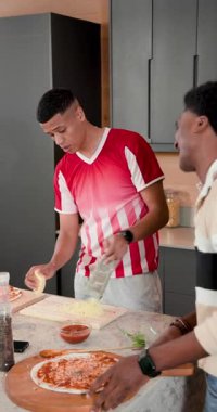 Çeşitli erkek arkadaşlar selfie kaydedip pizza yapmak için hamur üzerinde peynir rendeliyorlar. İşbirliği, yoldaşlık, aşçılık, hazırlık, modern yaşam tarzı, dikey video