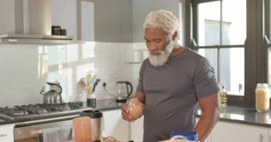 Mutfak tezgahında blender 'ı görürken, kıdemli Afrikalı Amerikalı bir adam cama smoothie dökerken, yudumlarken. Sağlıklı, beslenme, yaşam tarzı, modern, iç mekan, sağlık, rahatlama.