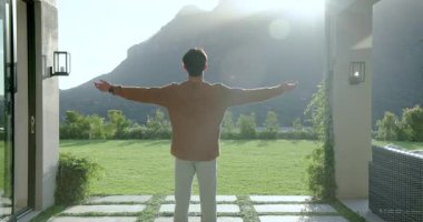 Asyalı bir adam pergola avlu eşiğine adım atıyor, kollarını yukarı doğru uzatarak sabah manzarası için. Sağlık, sükunet, doğa, dinginlik, açık hava, yaşam tarzı, farkındalık
