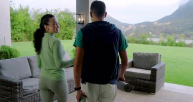 Spor giyimli bir çift ellerinde hasırlar ve şişelerle terasa çıkıp antrenman hazırlıyor. Spor, açık hava, yaşam tarzı, gündelik, rahatlama, manzara, sağlık.