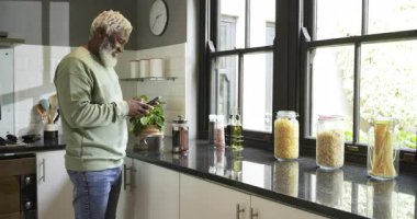 Olgun Afro-Amerikan adam akıllı telefonları kaydırıyor, demliyor, mutfakta Fransız kahvesini yudumluyor. Çağdaş, rahat, aromatik, yaşam tarzı, tasarım, yerli, rahatlama