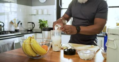 Muz görmek, kıdemli adamın süt dökmesi sonra da mutfak adasında sallamak için protein tozu alması. Sağlık, beslenme, yaşam tarzı, modern, sağlık, sağlık, hazırlık