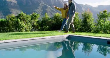 Çimenlikteki havuzun yanından geçen çift, dağ tepelerini görüyor, el ele tutuşurken işaret ediyor ve sohbet ediyorlar. Açık hava, boş zaman, manzara, sükunet, yaşam tarzı, resim, doğa.