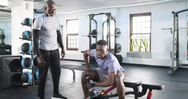 Afrikalı Amerikalı antrenör müşterinin beden eğitimi dersinde halteri kaldırıp göğüs germesi için işaret veriyor. Zindelik, güç, antrenman, spor salonu, sağlık, motivasyon.