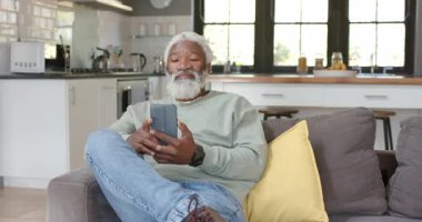 Afro-Amerikan son sınıf öğrencisi erkek evdeki kanepede akıllı telefonlara dokunmaya ve kaydırmaya tepki veriyor. Yaşlılık, rahatlama, modern, teknoloji, yaşam tarzı, konfor, mutluluk