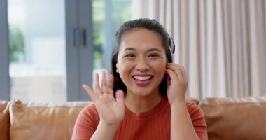 Aşağıya baktıktan sonra, Asyalı bir kadın evdeki özelliklerini göstermeden önce kablosuz kulaklık takıyor. Teknoloji, yaşam tarzı, modern, konfor, iletişim, rahatlama, canlı