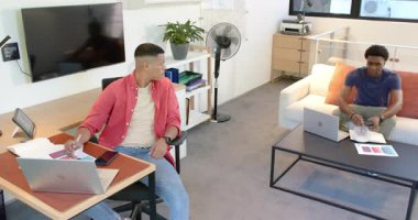 Çeşitli erkek iş arkadaşları kulaklıkları çıkarıyor, ofis masasına yürüyor ve belgeleri sınıflandırıyor. İşbirliği, birlikte çalışma, dijital, takım çalışması, modern, iletişim, üretkenlik