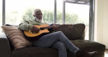 İlk akoru çaldıktan sonra koltukta akustik gitar çalan kıdemli Afrikalı Amerikalı adam. Müzisyen, boş zaman, geleneksel, halk, kırsal, düşünceli, akustik