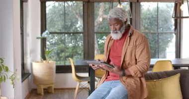 Kıdemli Afro-Amerikalı adam, oturma alanındaki tablet, tıkırtı, araklama, tarama uygulamaları üzerinde dinleniyor. Teknoloji, yaşam tarzı, modern, ev, rahatlama, bağlılık, iç mekan